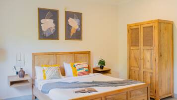 Una camera da letto con un letto di legno, un comodino con una lampada, un armadio e due dipinti astratti alle pareti.