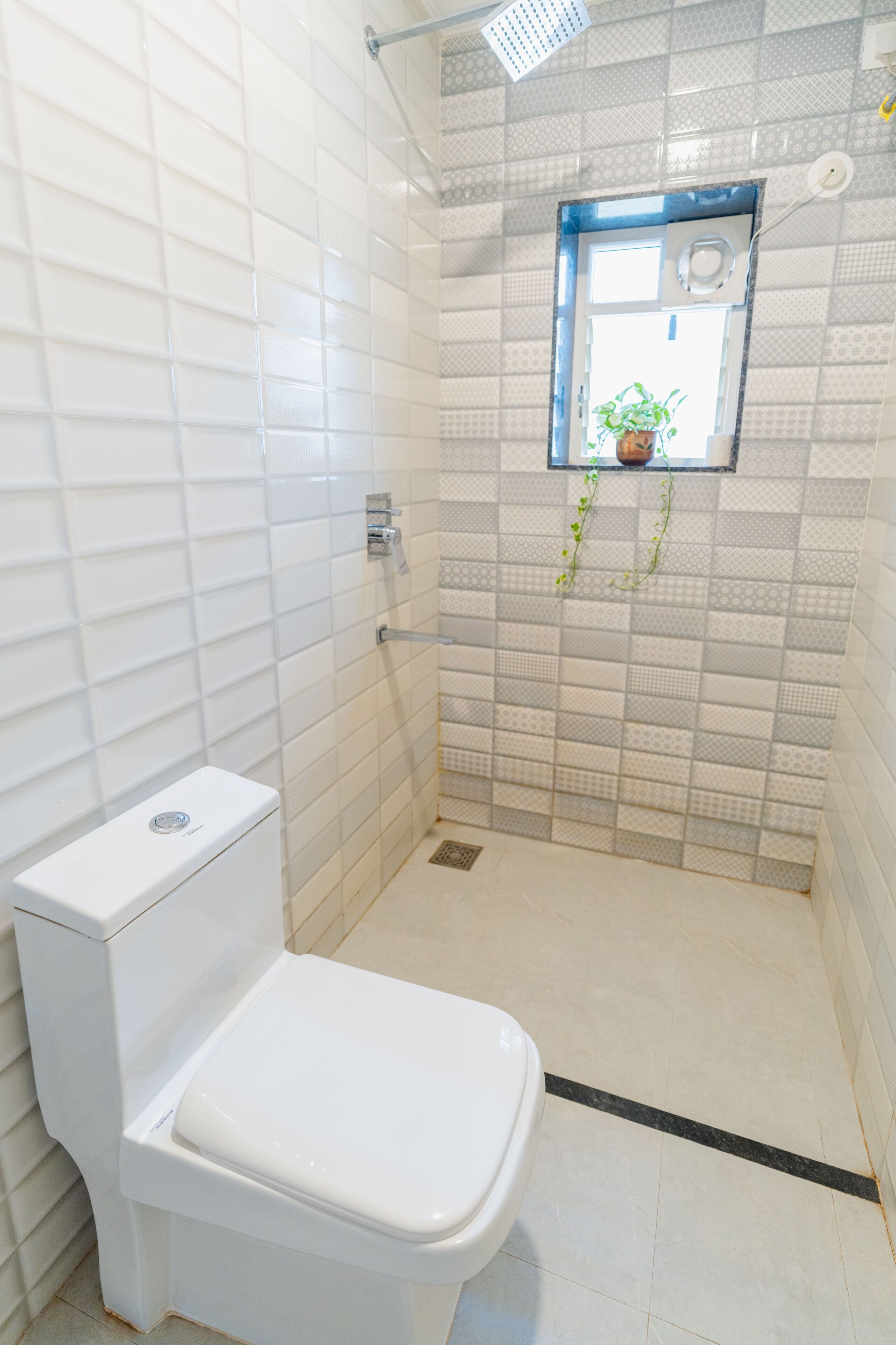 A bathroom with a white toilet, a shower, and a small window with a plant.
