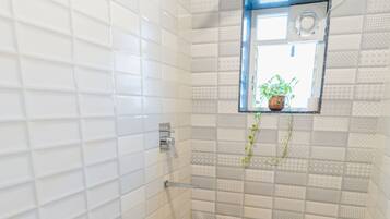 Un baño con inodoro blanco, ducha y una pequeña ventana con una planta.