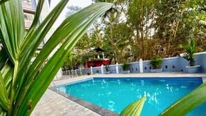 A swimming pool with a tiled deck, surrounded by a low wall and potted plants. - Mona Collective at Serenova (Calangute)