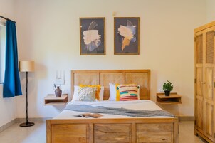 A neatly arranged bedroom with a wooden bed, a bedside table with a lamp, a nightstand with a vase, and a wardrobe.