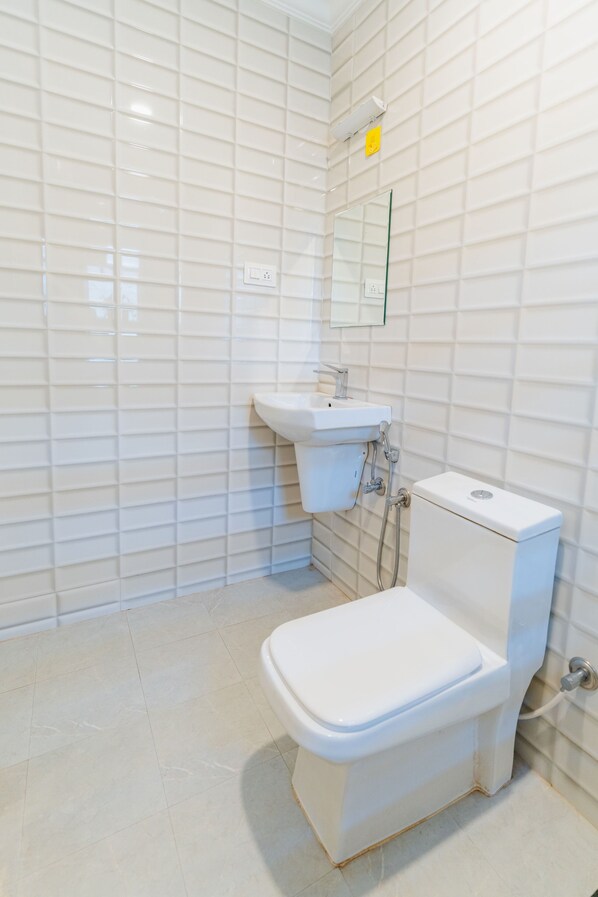 A modern bathroom with white tiled walls, a white sink, and a toilet. - Mona Collective at Serenova (Calangute)