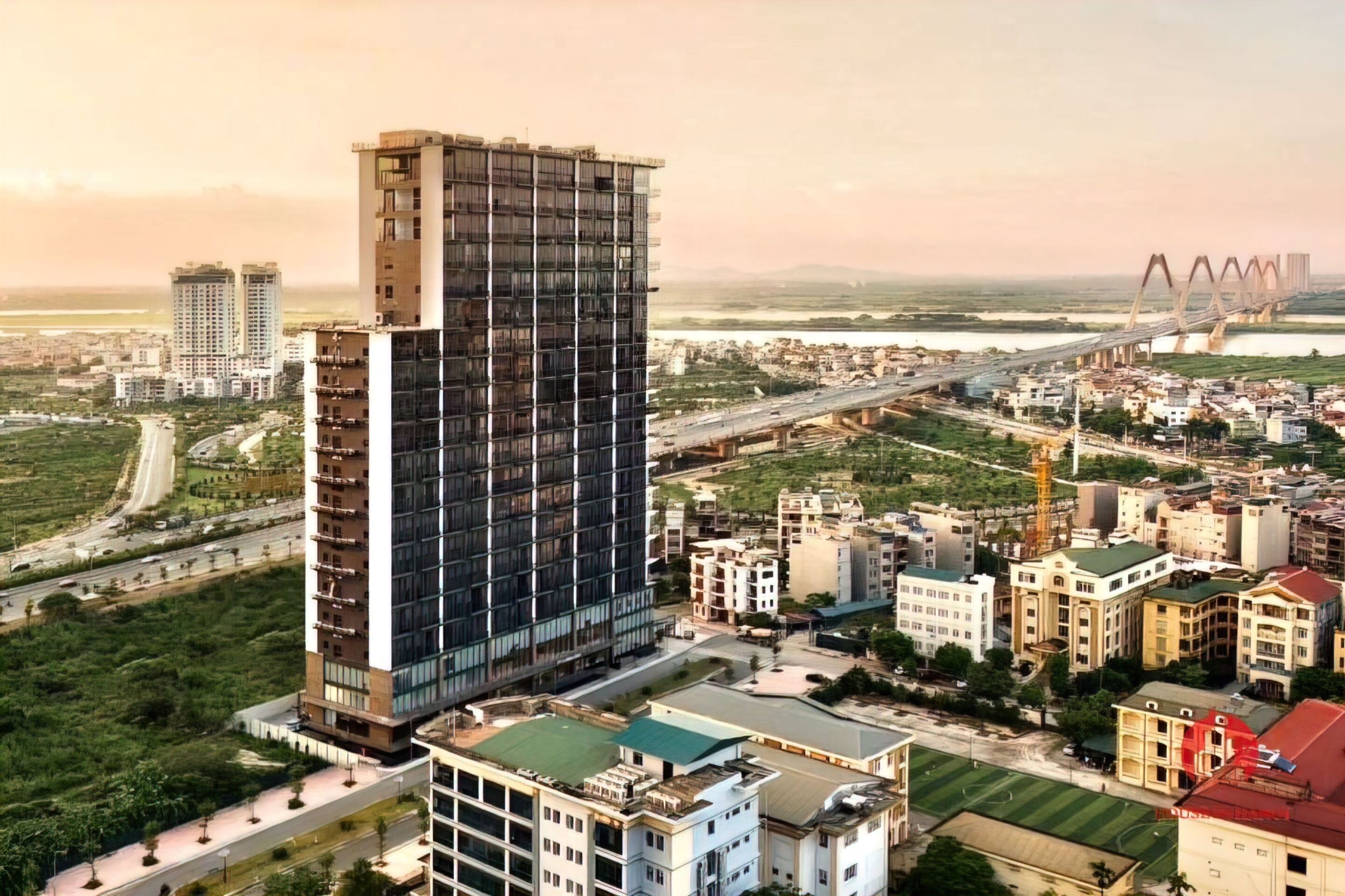 A high-rise building with a modern design, surrounded by a mix of residential and commercial buildings, with a bridge in the background.