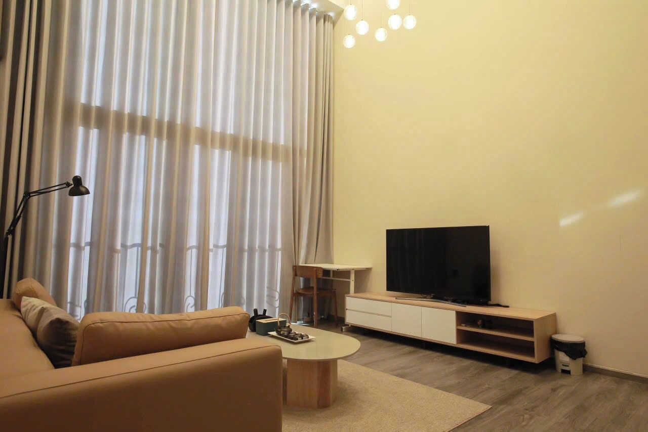 En moderne stue med sofa, sofabord, fjernsyn og gardiner.