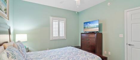 A bedroom with a bed, a dresser, a ceiling fan, a TV on a stand, and a window with blinds.