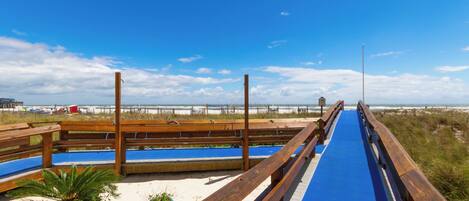 A wooden boardwalk leading to a beach with a clear sky.
