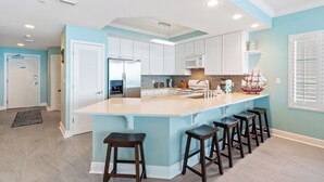A modern kitchen with white cabinets, a large island with bar stools, and a microwave. - San Carlos 1501 (Gulf Shores)