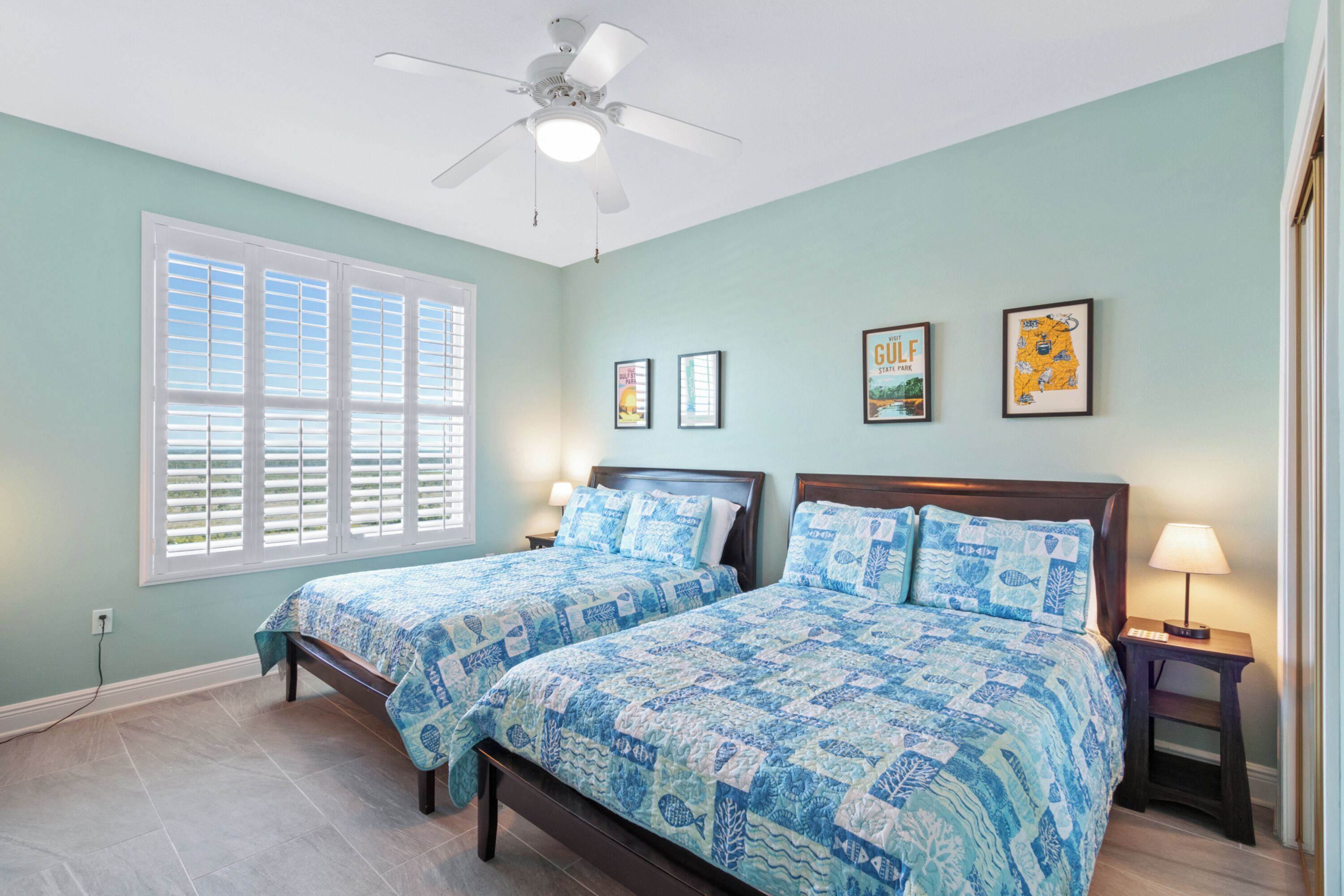 A bedroom with two beds, a ceiling fan, and a window with shutters.