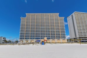 A high-rise hotel with multiple balconies, a beach in the foreground, and a clear blue sky. - San Carlos 1501 (Gulf Shores)