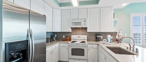 A modern kitchen with white cabinetry, stainless steel appliances, a built-in microwave, and a large sink.
