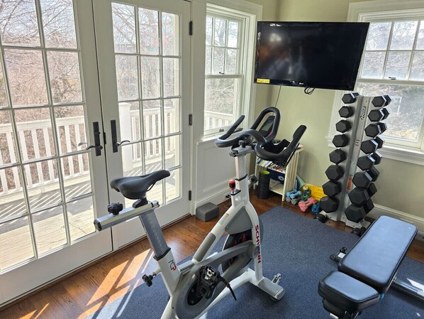 Un gimnasio en casa con una bicicleta estática, una banca, mancuernas y un televisor montado en la pared.