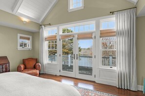 Un dormitorio con una ventana grande, una silla, una cama y un aparador.