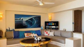 A living room with a large painting, a flat-screen TV, a ceiling fan, and a sofa with decorative pillows.