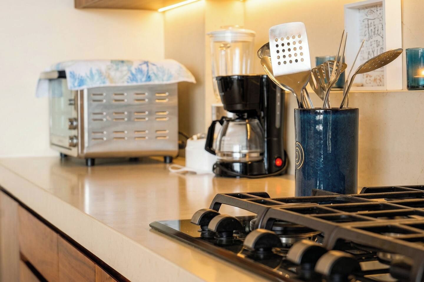 Eine Küche mit einem Gasherd, einer Kaffeemaschine, einem Toaster und einem blauen Behälter mit Besteck.