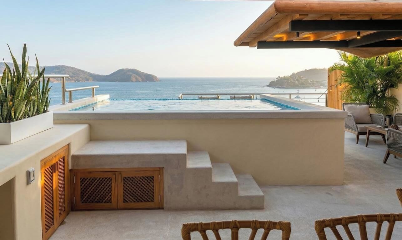 An infinity pool with a view of the sea, steps leading to the pool, and outdoor seating.
