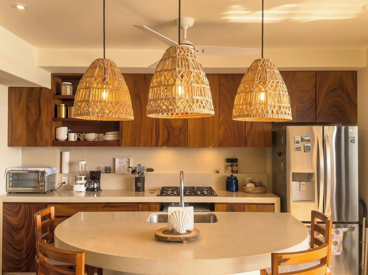 A modern kitchen with a round dining table, pendant lights, wooden cabinets, and stainless steel appliances.