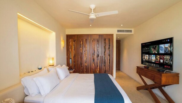 Habitación de hotel con cama, mesita de noche, lámpara, televisor y un panel divisor de madera.