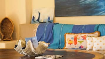 A room with a wooden coffee table, a card game, a decorative shell, a sailboat painting, and a sofa with patterned cushions.