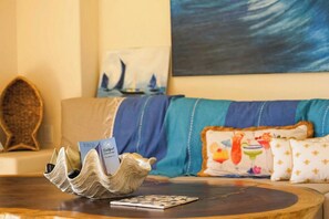 A room with a wooden coffee table, a card game, a decorative shell, a sailboat painting, and a sofa with patterned cushions. - Luxury Penthouse at Aura del Mar (Zihuatanejo)