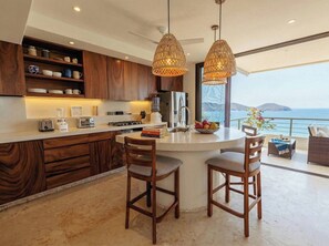 A modern kitchen with a central island, wooden cabinets, and a view of the sea.