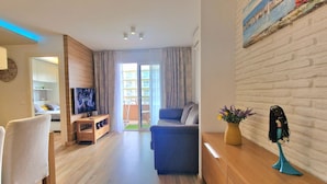 Ein modernes Wohnzimmer mit Sofa, Fernseher, Holzboden und Blick durch eine Glastür auf einen Balkon.