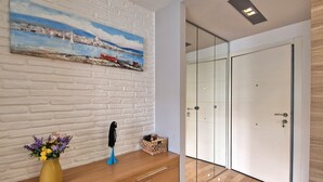 Ein modernes Zimmer mit einer weißen Ziegelwand, einem Gemälde einer Küstenlandschaft, einer Holzkommode und einer Glastür.
