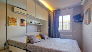 Ein modernes Schlafzimmer mit einem Bett, Einbauschränken, einem Fernseher und einem Fenster mit Vorhängen.