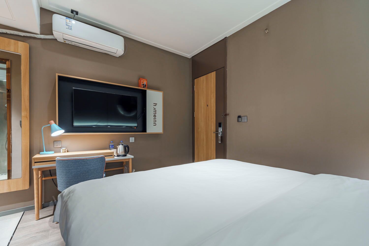 A hotel room with a bed, a desk with a chair, a television, and an air conditioning unit.