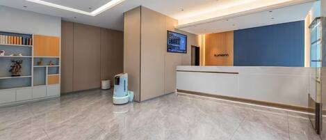 A modern reception area with a clean, minimalist design, featuring a reception desk, a digital display, and a well-organized shelving unit.