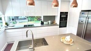 Cozinha moderna com armários brancos, eletrodomésticos de aço inoxidável e luminárias pendentes em cobre.