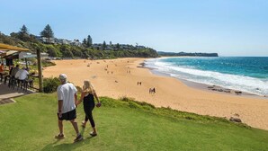 Uma praia com área gramada e um edifício com mesas ao ar livre.