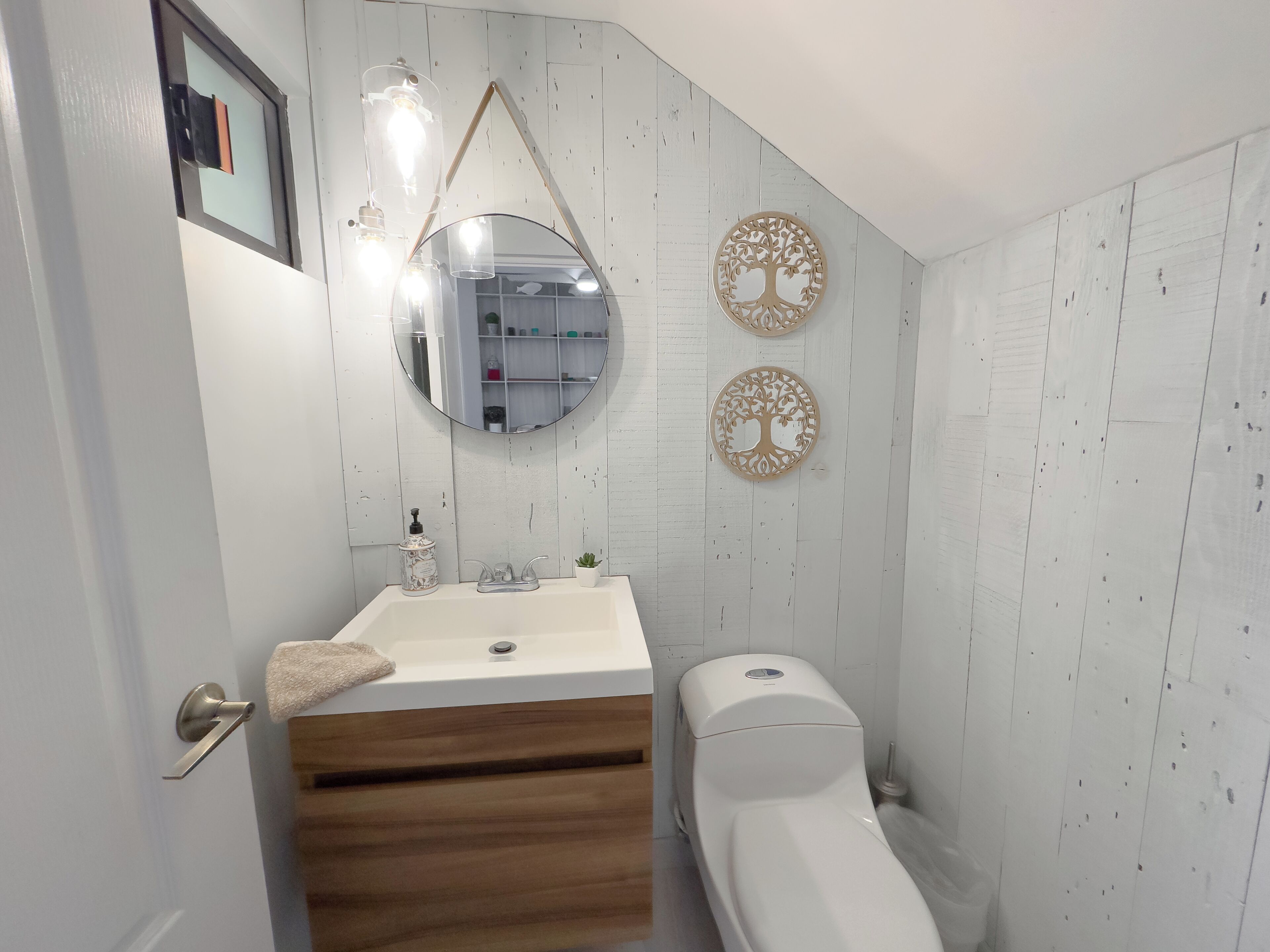 Un bagno con un mobile bagno in legno, un lavandino bianco, uno specchio e due pannelli decorativi a parete.