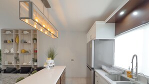 A modern kitchen with a central island, built-in shelves, and a stainless steel refrigerator.