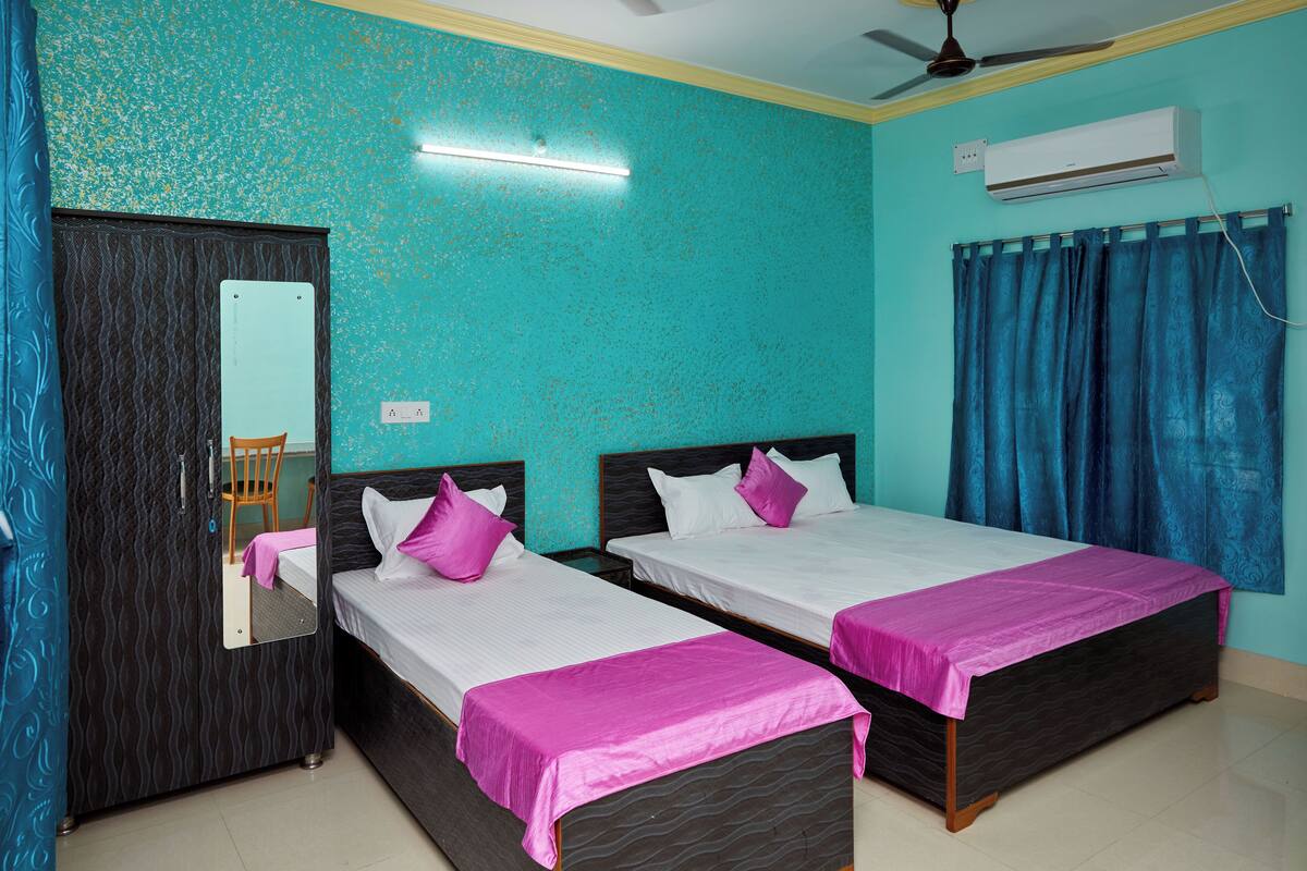 A room with two beds, a wardrobe, a mirror, an air conditioning unit, and a ceiling fan.