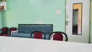 A waiting area with a blue sofa, red chairs, a white table, and a door with a mirror. - Deb Guest House (Barakpur)