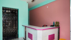 A reception desk with a pink and white color scheme, a black metal gate, and two yellow stools. - Deb Guest House (Barakpur)