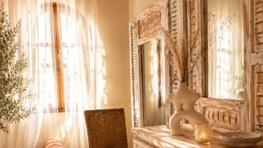 Una habitación con un espejo grande, una silla de mimbre, un banco verde y un jarrón decorativo.