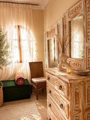 A room with a large mirror, a wicker chair, a green bench, and a decorative vase.