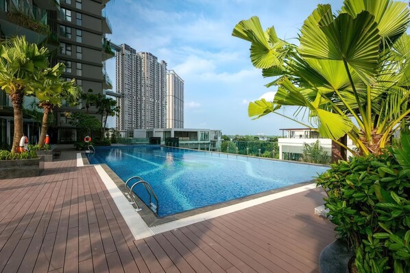 A swimming pool with a wooden deck, surrounded by greenery and modern buildings. - Sol Forest Ecopark Apartments (Phung Cong)