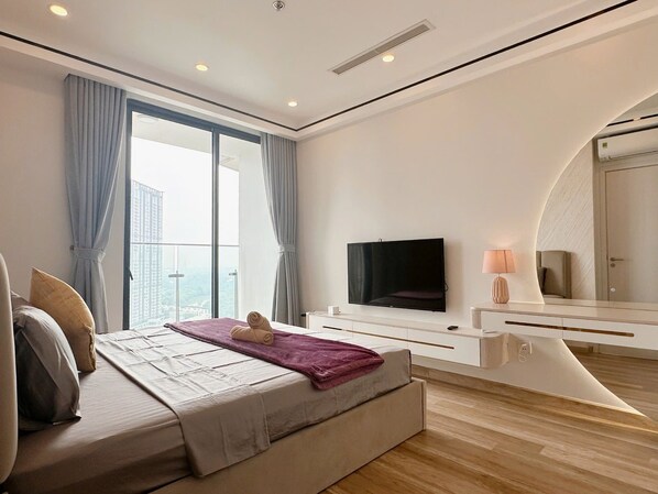 Una habitación de hotel moderna con una cama grande, un televisor de pantalla plana, un escritorio y un ventanal con cortinas.