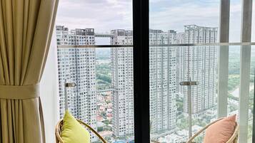 A balcony with wicker chairs and cushions, a view of high-rise buildings, and a clear sky.