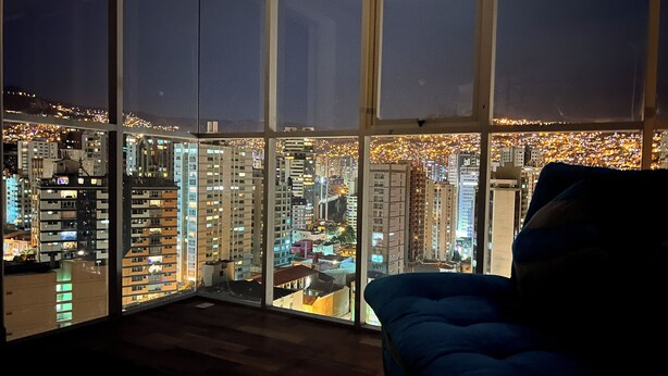 Korkeassa kerroksessa sijaitseva huone, jossa on suuret ikkunat, joista avautuu näkymä kaupungin ylle yöllä.