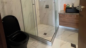 Moderni kylpyhuone, jossa on lasiseinällä varustettu suihku, wc ja pesuallas, jonka yhteydessä on tilaa hygieniatuotteille.