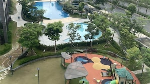 A residential complex with a swimming pool, playground, and surrounding greenery.