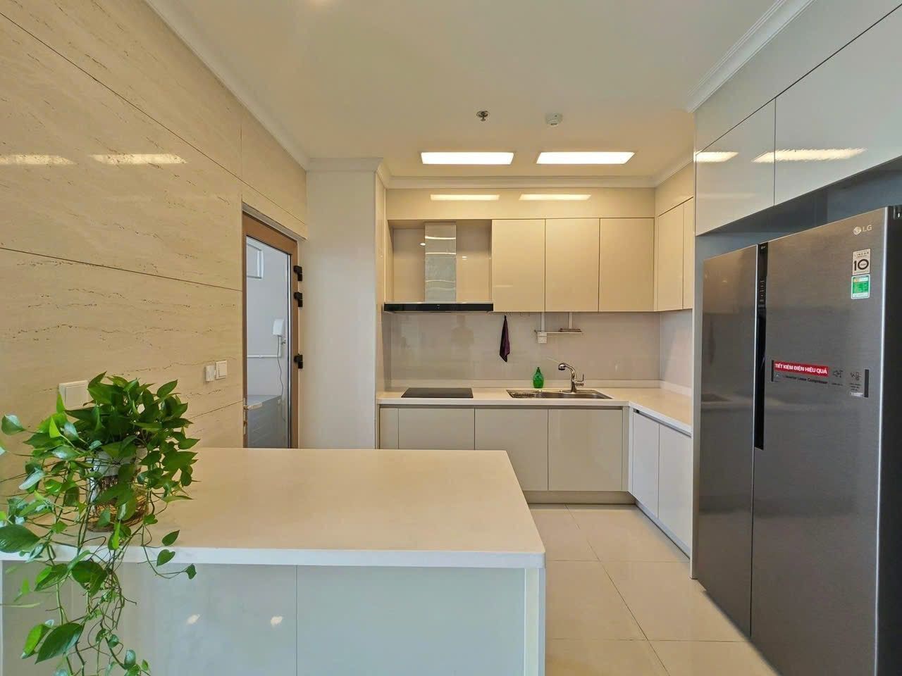 A modern kitchen with white cabinetry, a stainless steel refrigerator, and a small island with a plant.