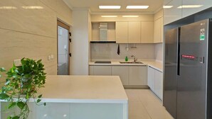 A modern kitchen with white cabinetry, a stainless steel refrigerator, and a small island with a plant.