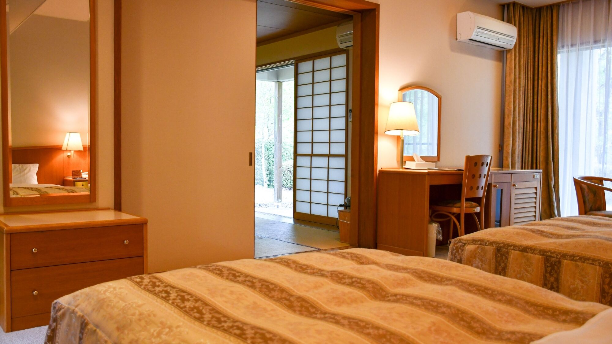 Habitación de hotel con dos camas, un escritorio, una silla, un espejo y un equipo de aire acondicionado.