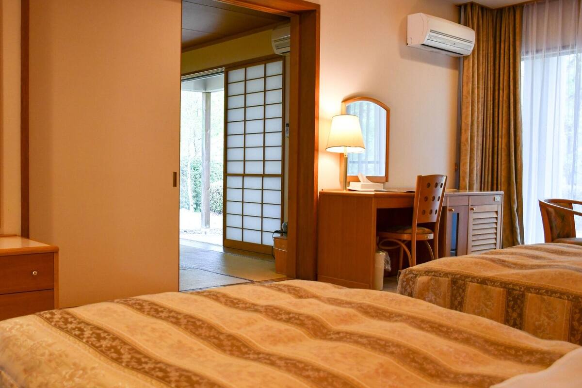 Quarto de hotel com duas camas, uma escrivaninha, uma cadeira, um espelho e um ar condicionado.