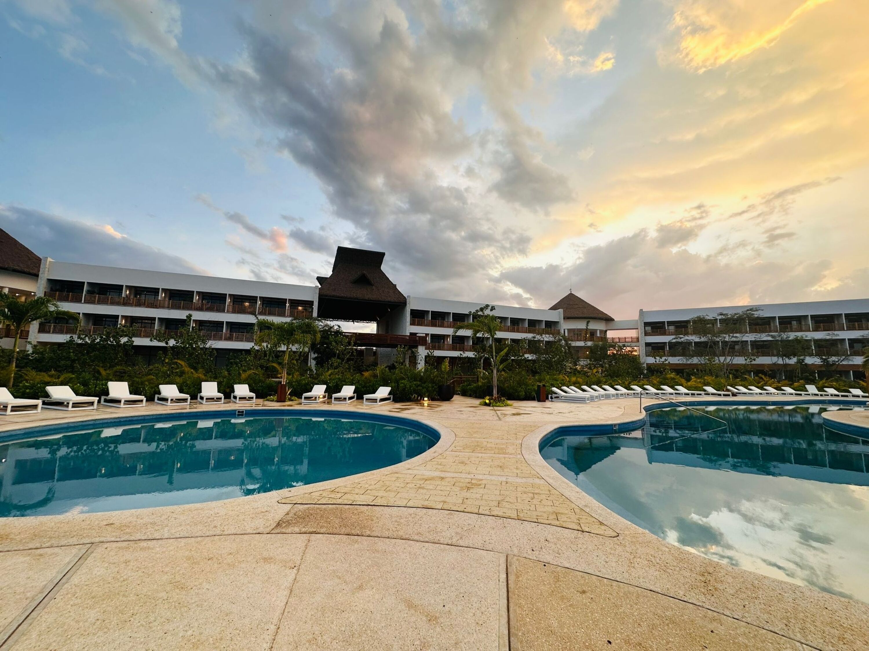 A resort pool area with two large pools, lounge chairs, and a building with multiple balconies.