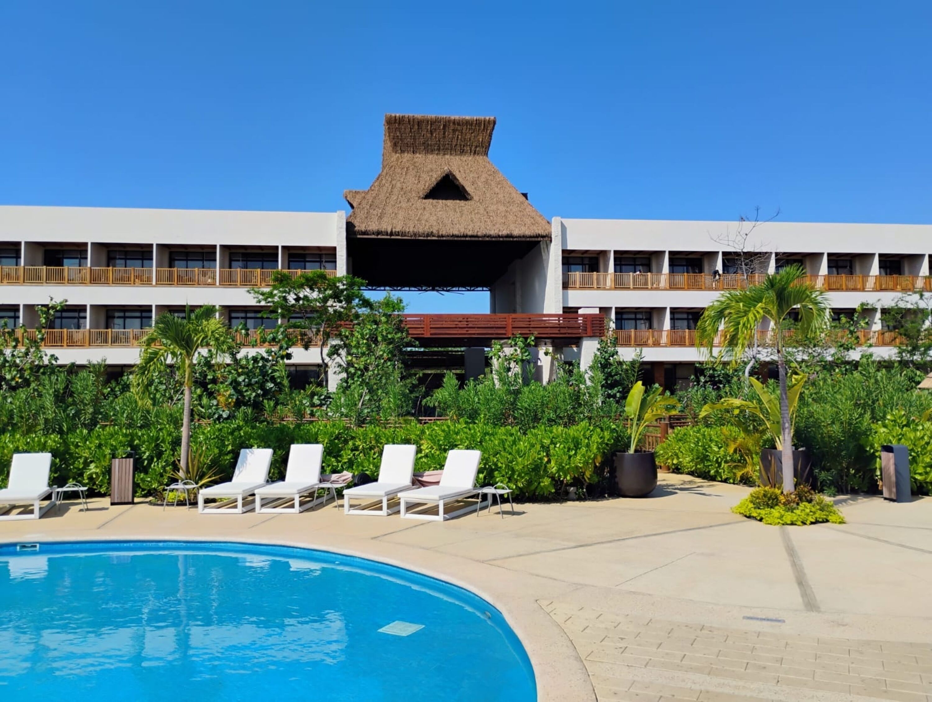 Ein Hotel mit Schwimmbad, weißen Liegestühlen und üppiger Bepflanzung.